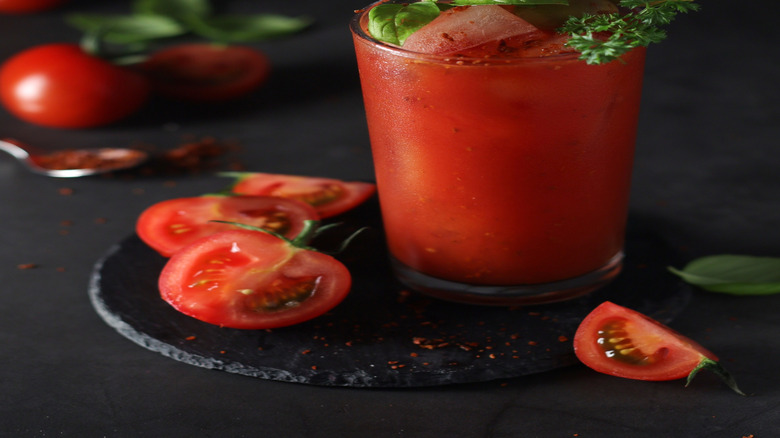 An iced Bloody Mary with basil, a pickle, and a cherry tomato garnish