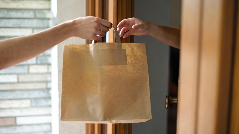Someone handing grocery bag to another person.