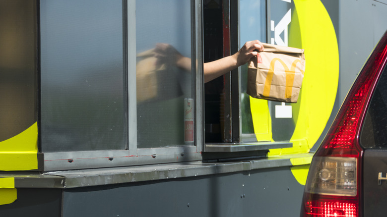An employee hands a McDonald's bag out the drive-thru window