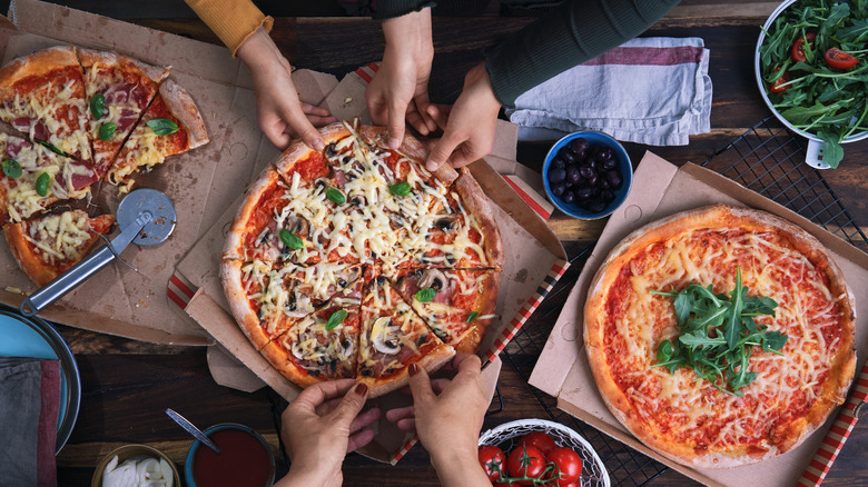 Hands grabbing slices of pizza out of takeout boxes