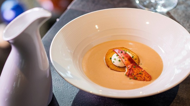 A bowl of lobster bisque and a small pitcher sit on a table at Eddie V's Prime Seafood