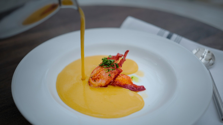 Lobster bisque is poured into a bowl around pieces of lobster