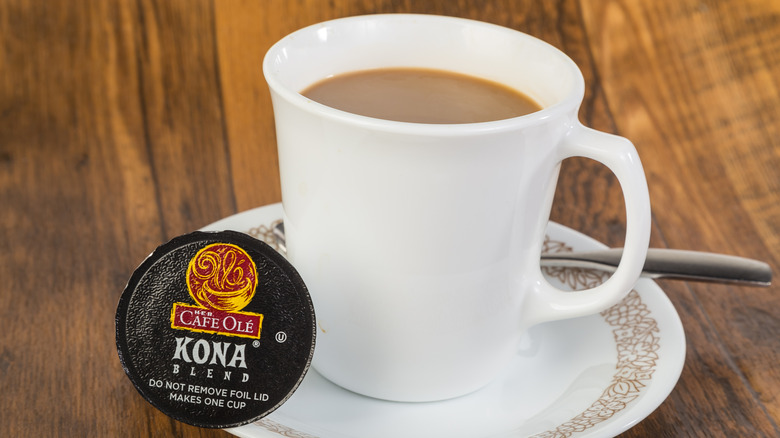 white mug of hot coffee next to K-cup on wooden table