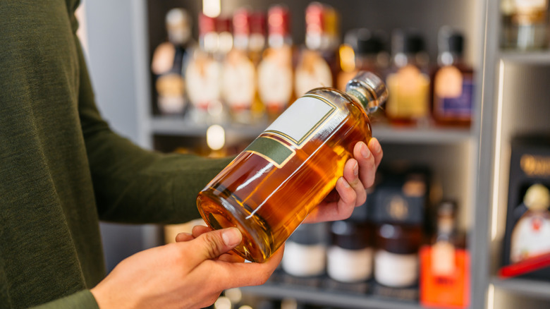 Man looking at whiskey bottles in a liquor store.