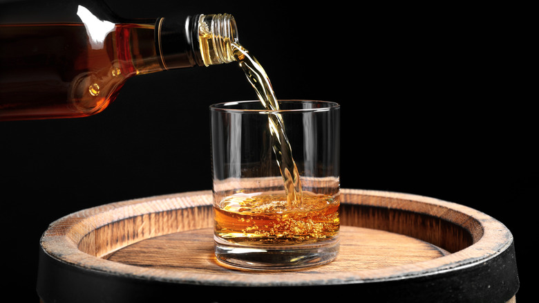 Bourbon poured from bottle into glass on wooden barrel