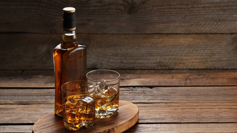 Whiskey with ice cubes in glasses and bottle on wooden table