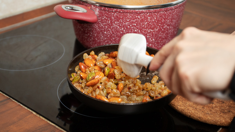 Almonds pistachios and raisins frying in butter in a shallow pan