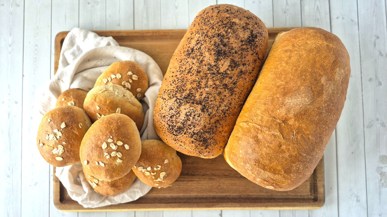 Two loaves of bread and several bread rolls on a wooden cutting board
