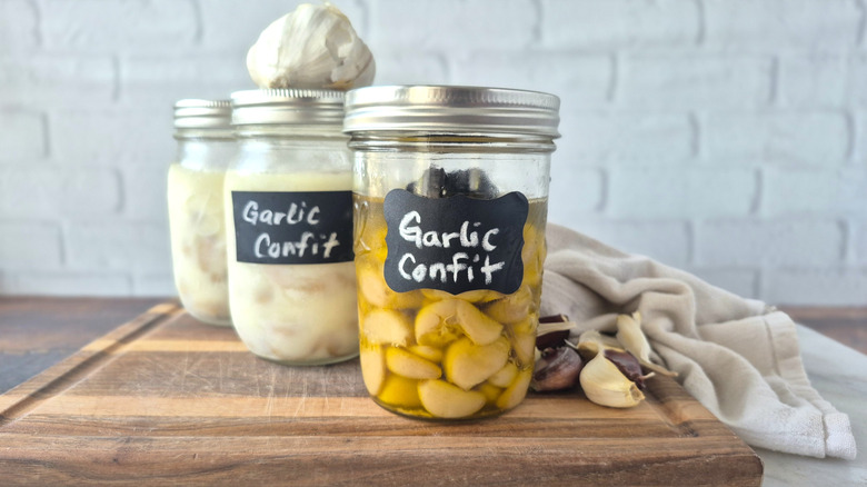 a jar of garlic confit with several jars of frozen confit behind it on a cutting board