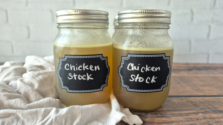 two jars of chicken stock on a wooden surface with a white towel