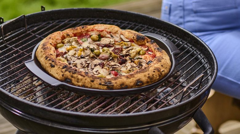 A pizza rests on a Peugeot Grill to Table Ceramic Pizza Stone over a grill
