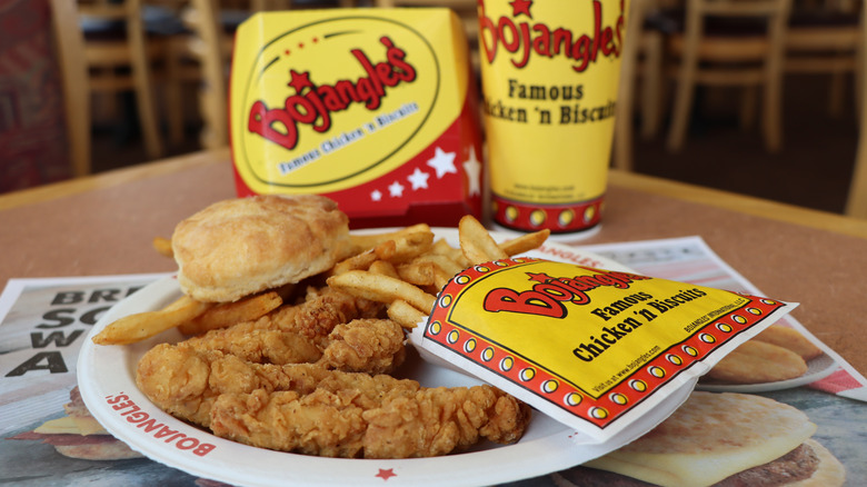 Bojangles chicken, biscuit, and fries on a white plate with Bojangles cup, container, and flyer positioned on the table
