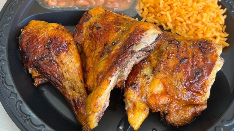 El Pollo Loco chicken on a black plate next to rice and beans