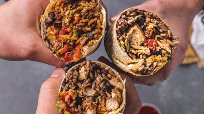 Three people's hands holding open burritos from a top-view