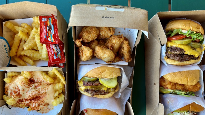 Shake Shack fries, chicken bites, and burgers in cardboard containers on a blue-green table