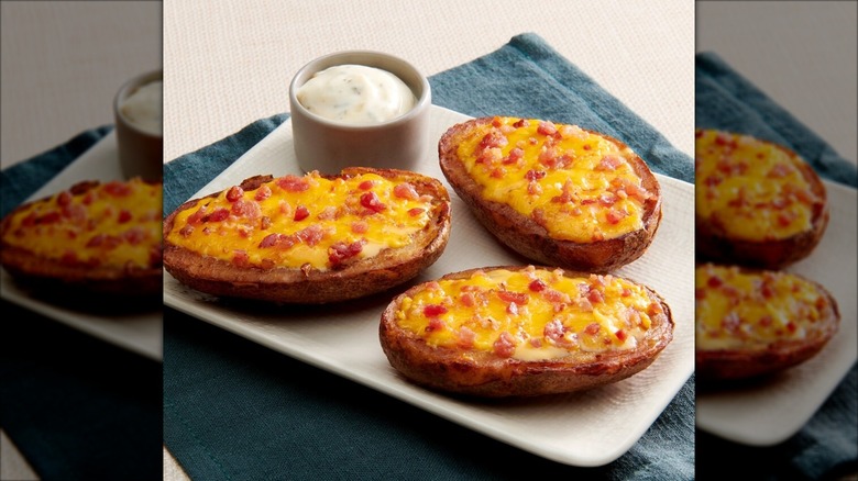 Three prepared Snapps Potato Skins on a white serving dish with a ramekin of dipping sauce.