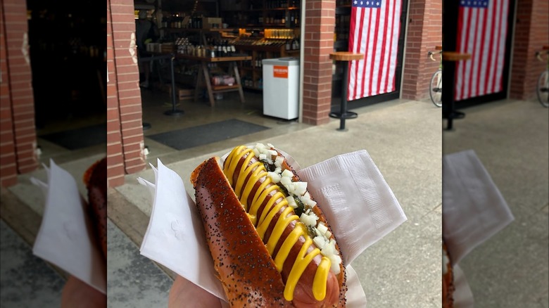 A person holding an Honor Market hot dog in front of the store opening
