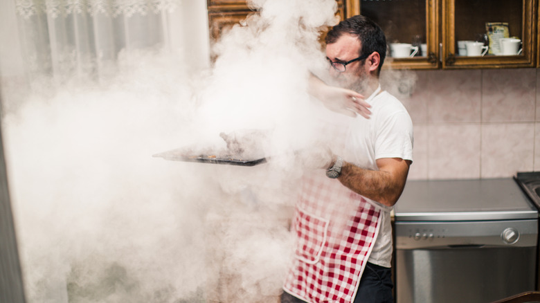 person waving at smoky oven 