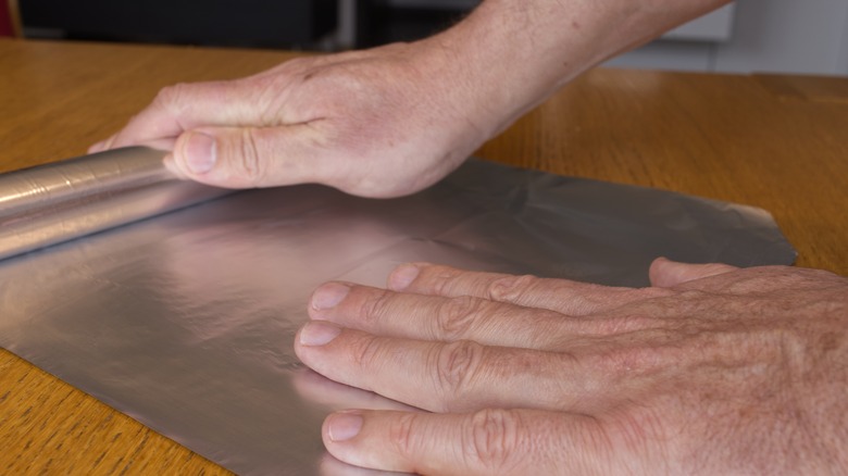 person rolling out aluminum foil