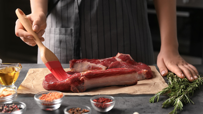 person brushing steak with oil
