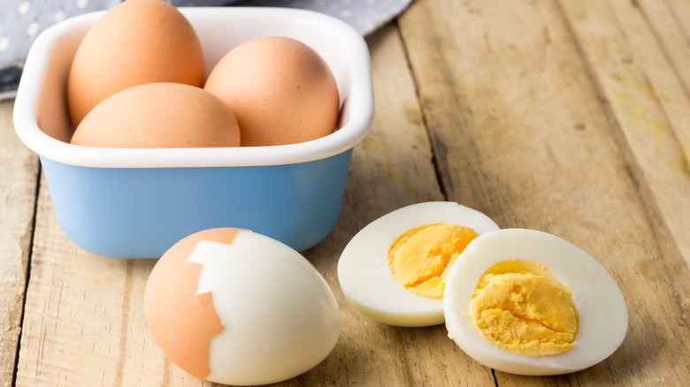 whole and partly peeled hard-boiled eggs on wooden table