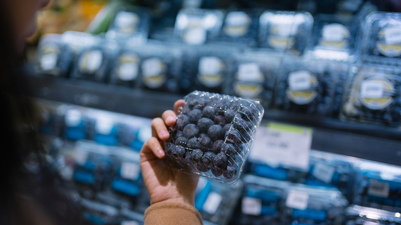 Woman examining the underside of a clamshell full of blueberries
