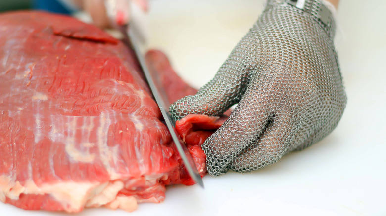 A butcher trimming meat with a knife on a cutting board