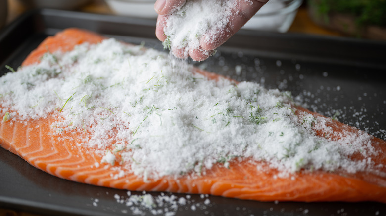 A person covering a salmon filet in salt to make gravlox