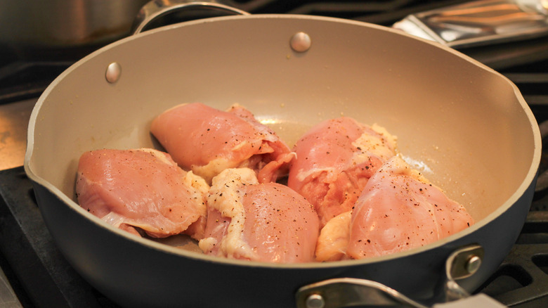 Raw chicken thighs cooking in a frying pan