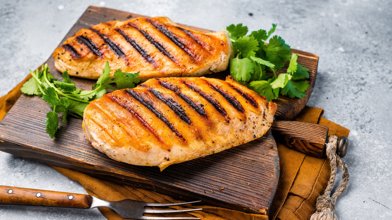 Two grilled chicken breasts on a cutting board with garnish