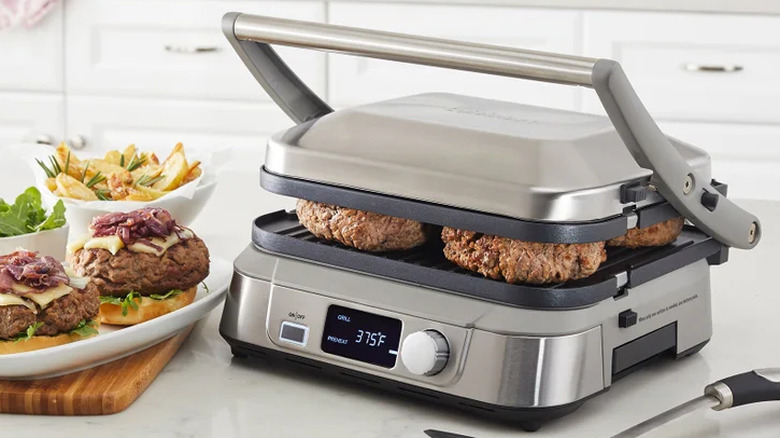 Cuisinart Digital Griddler cooking hamburgers with digtial screen indicating 375 degrees on countertop next to plate of cooked burgers