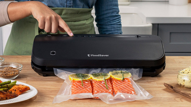 woman's hand pressing a button on a FoodSaver Preserve Vacuum Sealer machine to seal salmon filets on kitchen countertop