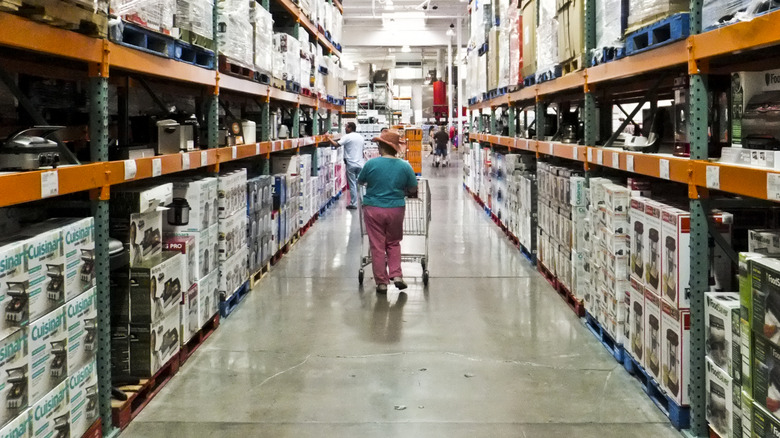 woman in cowboy hat walking through Costco kitchen appliance aisle with shopping cart