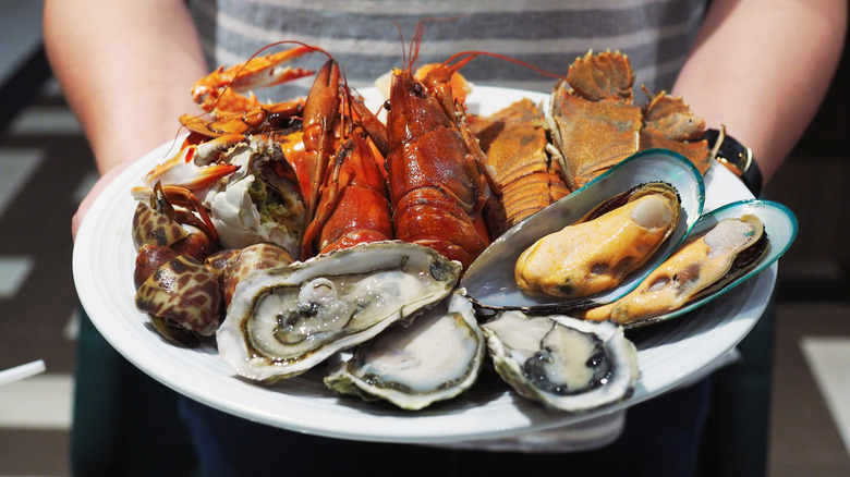 A person holds a plate filled with a variety of seafoods