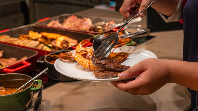 A person puts seafood on their plate at a seafood buffet