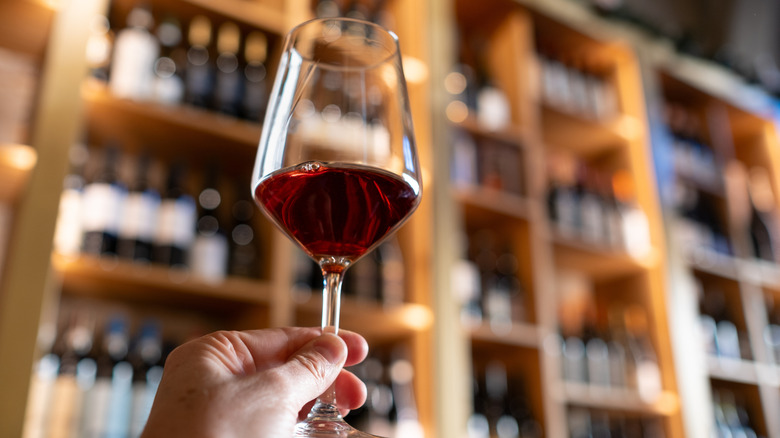 A glass of red wine being held up in front of shelves of bottles
