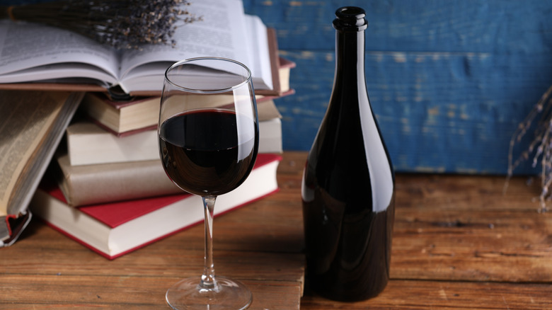 A glass of red wine next to a bottle with books in background