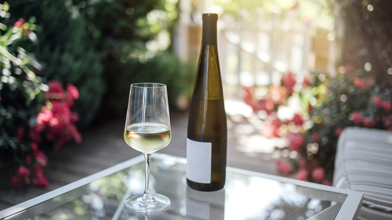 A glass of white wine next to a wine bottle on a table outdoors