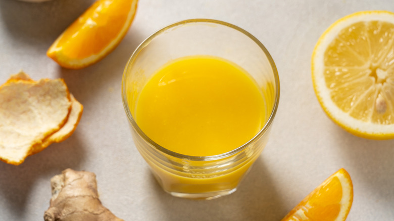 Glass of juice with fresh ginger, orange, and lemon