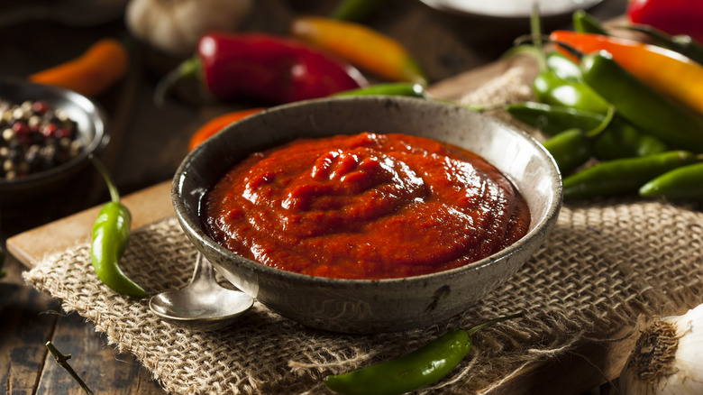 red sriracha in a bowl with peppers on table