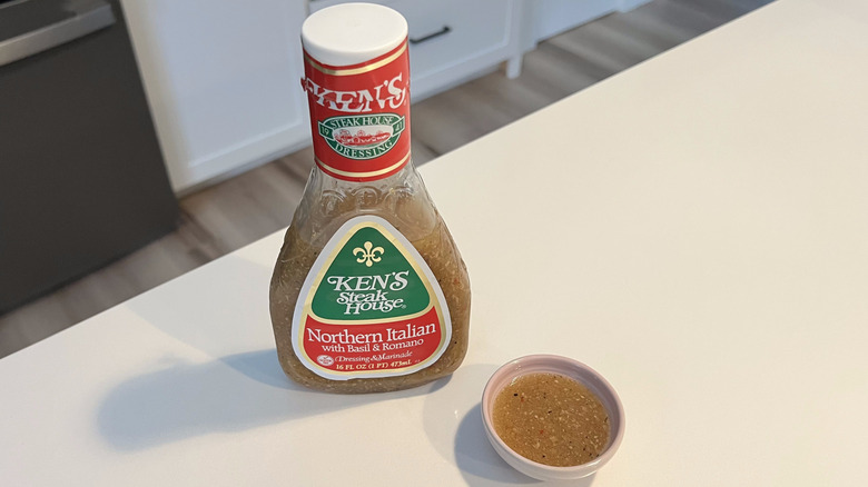 A bottle of Ken's Steakhouse Northern Italian dressing sitting on a white kitchen counter next to a small condiment dish filled with the dressing
