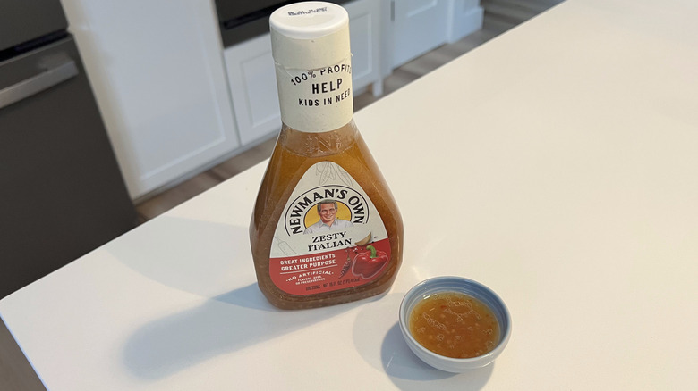 A bottle of Newman's Own Zesty Italian sitting on a white kitchen counter next to a small condiment dish filled with the dressing