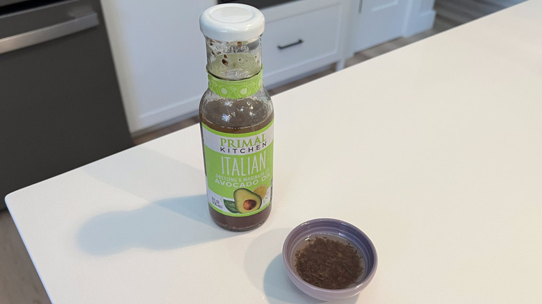A bottle of Primal Kitchen Italian sitting on a white kitchen counter next to a small condiment dish filled with the dressing