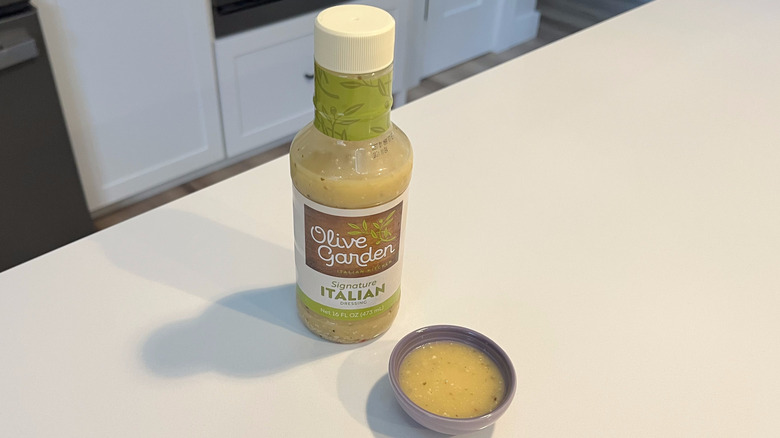 A bottle of Olive Garden Signature Italian sitting on a white kitchen counter next to a small condiment dish filled with the dressing
