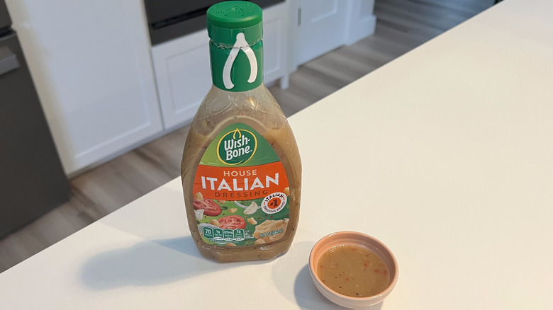 A bottle of Wishbone House Italian Dressing sitting on a white kitchen counter next to a small condiment dish filled with the dressing