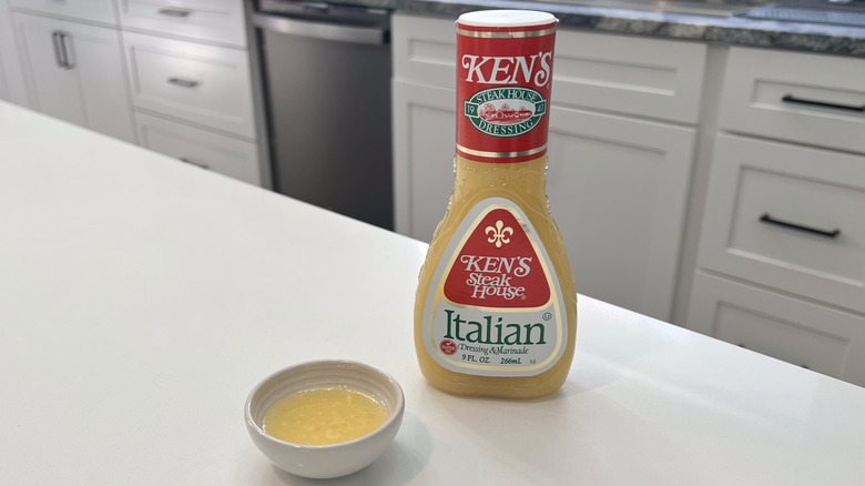 A bottle of Ken's Steakhouse Italian sitting on a white kitchen counter next to a small condiment dish filled with the dressing