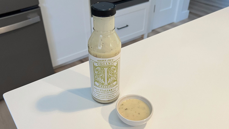A bottle of Trader Joe's Organic Italian Dressing sitting on a white kitchen counter next to a small condiment dish filled with the dressing