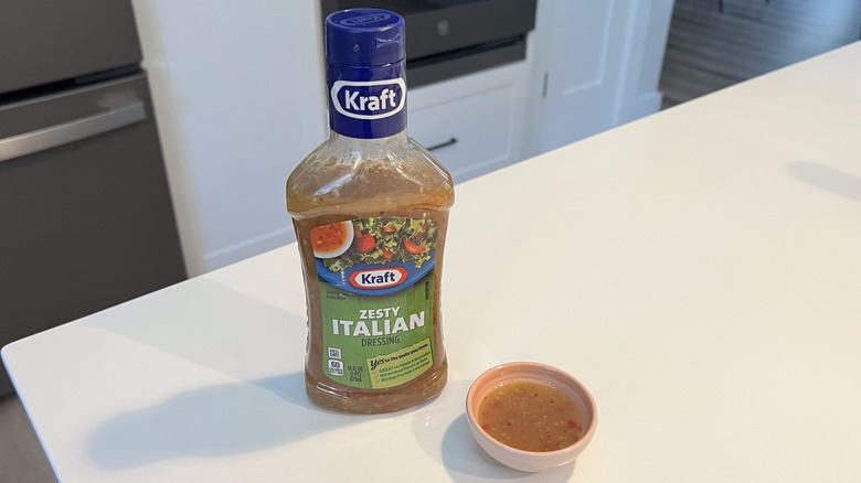 A bottle of Kraft Zesty Italian sitting on a white kitchen counter next to a small condiment dish filled with the dressing