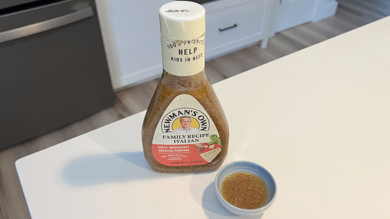 A bottle of Newman's Own Family Recipe Italian sitting on a white kitchen counter next to a small condiment dish filled with the dressing