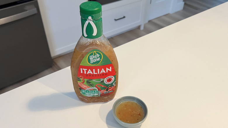 A bottle of Wishbone Italian Dressing sitting on a white kitchen counter next to a small condiment dish filled with the dressing